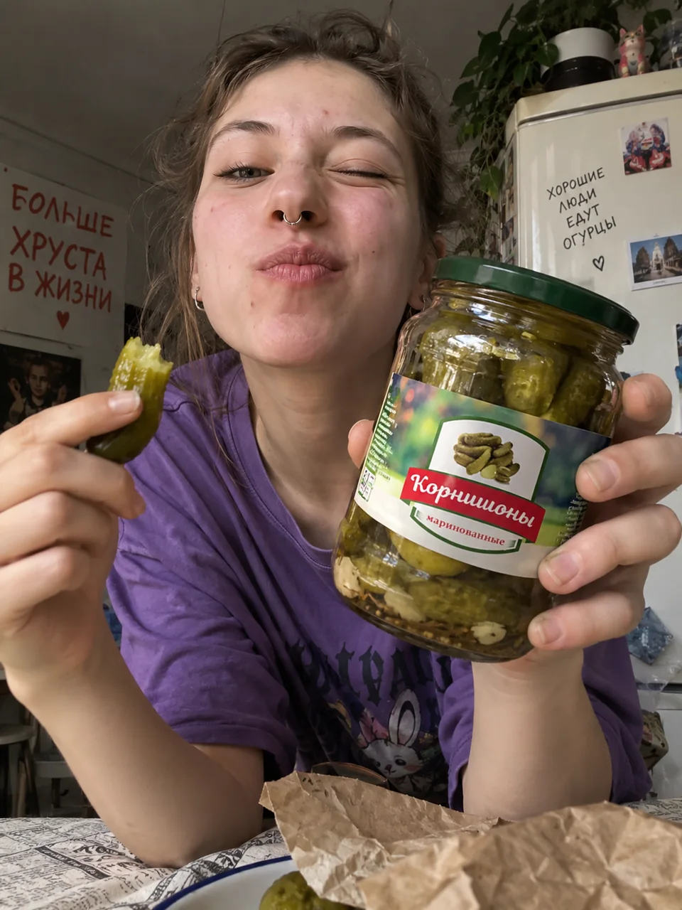 Девушка с банкой маринованных корнишонов и надкусанным огурцом на кухне